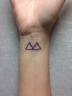 a small tattoo on the wrist of a person with mountains in the background and an arrow at the bottom