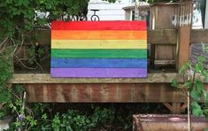 a rainbow painted wooden sign sitting on top of a wooden bench next to a tree