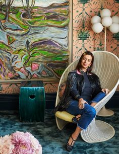 a woman sitting in a chair next to a painting on the wall and another flower vase