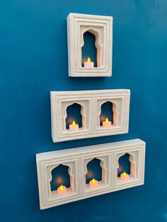 three white candles are lit in small niches on a blue wall with two smaller ones behind them