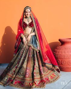 a woman in a red and blue lehenga standing next to an orange wall