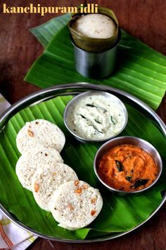 some food is on a metal plate with green leaves and sauces in small bowls