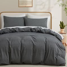 a bed with grey sheets and pillows in a room next to a potted plant