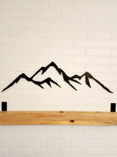 three metal mountains on a wooden shelf against a white brick wall in front of a fireplace