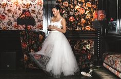 a woman in a white wedding dress standing next to a floral wallpapered room