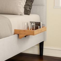 a bed with a white headboard and wooden tray on the bottom shelf next to it