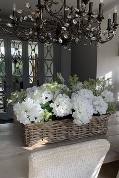 a dining room table with white flowers in a basket on the centerpiece and chandelier