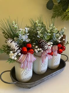 three mason jars filled with pine cones and christmas greenery are sitting on a tray