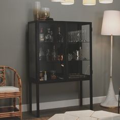 a glass cabinet with liquor bottles and glasses in it next to a lamp on the floor