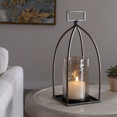 a candle is sitting in a glass container on a table next to a couch and potted plant