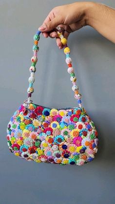 a hand holding a multicolored purse with beads