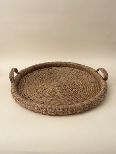 a round wicker tray with handles on a plain surface, ready to be used as a serving platter