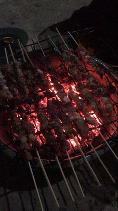 there are many skewers that are cooking on the bbq grill, and one is lit up with red light