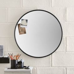 a round mirror hanging on the wall next to a pile of books and pencils