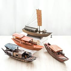 three models of boats sitting on top of a wooden table next to eachother