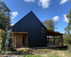 a black building with a wooden deck in front of it and trees around the yard