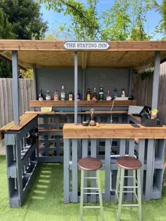 an outdoor bar made out of pallets with stools in the grass and some bottles on top