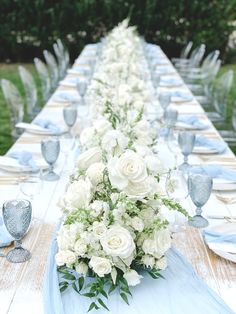 a long table with white flowers and blue napkins is set for an outdoor dinner