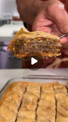 a person holding up a piece of food in front of a pan filled with pastries