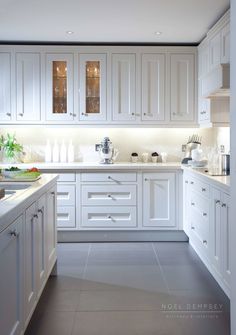 a large kitchen with white cabinets and counter tops is lit by recessed lights above the sink