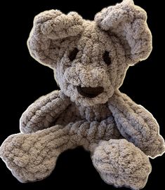 a gray teddy bear sitting up against a black background