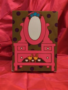 a pink vanity with polka dots and a mirror on it's side, sitting on a red sheet