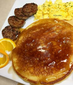 pancakes, scrambled eggs and sausage on a white plate with orange slices next to them