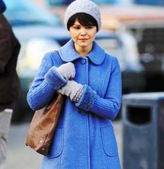 a woman in a blue coat is walking down the street with her hand on her purse