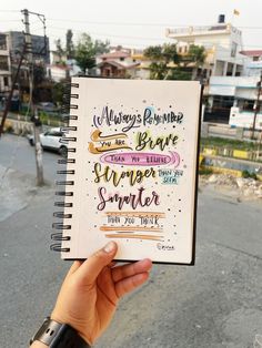 a hand holding up a notebook with writing on it in the middle of a street