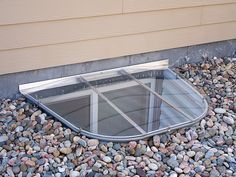 a glass window sitting on top of a pile of rocks next to a house wall