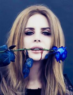 a woman with long blonde hair and blue eyes holds a rose in front of her face