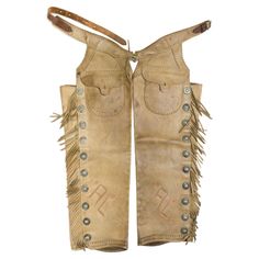 Vintage leather R.T. Frazier shotgun chaps with outside buck stitched pockets, fringe and conchos. Assume owner's initials or brand "AL." Maker marked. Leather is a light beige color with great patina. Would display nicely in a Western stye home. 36"L, 44" waist. Family Owned & Operated Cisco’s Gallery deals in the rare, exceptional, and one-of-a-kind pieces that define the history of America and the Old West. Our pieces range from American Indian to Cowboy Western and include original items of Wooly Chaps, Fur Chaps, Chaps Denim True American Brand, Assless Chaps Cowgirl, Leather Chaps American Legend Rider, Shotgun Chaps, Honesty And Integrity, Cow Boy, Western Cowboy