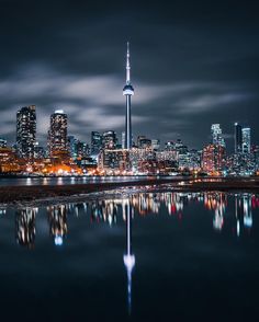 the city skyline is lit up at night with lights reflecting in the water and skyscrapers