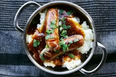 two sausages with gravy and mashed potatoes in a pan on a table