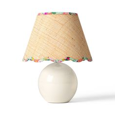 a white table lamp with a beige shade on it's base and colorful trim