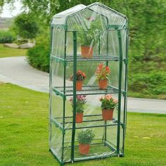 a green house with potted plants in it on top of the grass and trees