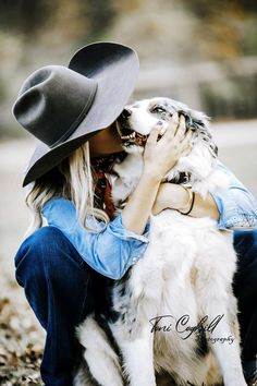 a woman is hugging her dog while wearing a cowboy's hat and sitting on the ground