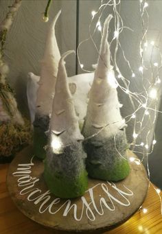 three white and green gnome hats sitting on top of a wooden table next to a christmas tree