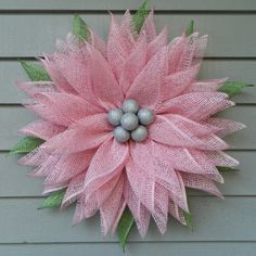 a pink flower with green leaves and silver balls on it's center is hanging from the side of a house