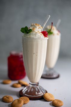 two glasses filled with milkshakes and cookies on a table next to each other