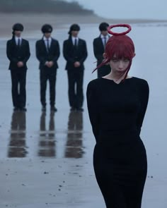 a woman in a black dress standing on the beach with other people wearing suits and ties