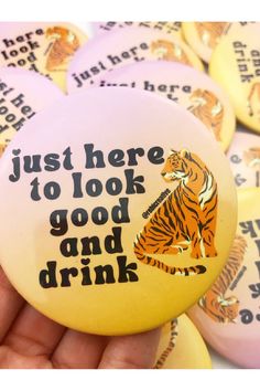 a hand holding a button that says, just here to look good and drink tiger