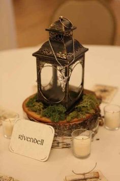 a small lantern is sitting on top of a moss covered tablecloth with candles and place cards