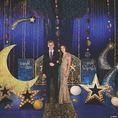 a man and woman standing in front of a backdrop with stars, moon and crescents