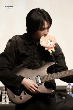 a young man holding an electric guitar while wearing a stuffed animal in his mouth and looking at the camera