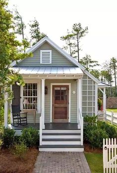 a small gray and white house with a porch, front door and steps leading up to it