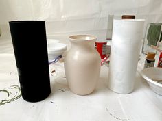 several different types of vases and bowls on a table with white cloth behind them