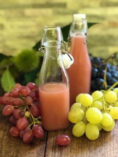 two bottles filled with orange juice next to grapes