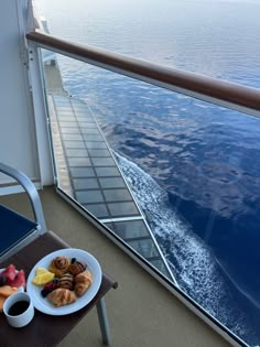 a plate of fruit and pastries on the deck of a cruise ship with water in the background