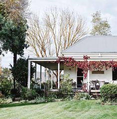 a small white house with red flowers on the front porch and covered in ivys